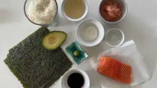 Wszystkie składniki do sushi: ryż, nori, łosoś, awokado, sos sojowy, wasabi, marynowany imbir i ocet ryżowy.
