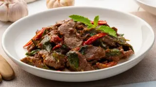 Aksamitne kawałki wołowiny po tajsku z bazylią i papryczką chili, podane w białej misce.