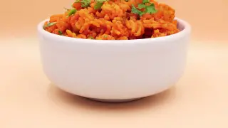 Pomarańczowy ryż z curry, posypany świeżą natką pietruszki, w białej miseczce.