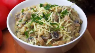 Pyszne risotto z pieczarkami, posypane startym serem i świeżą natką pietruszki, czeka w białej miseczce.
