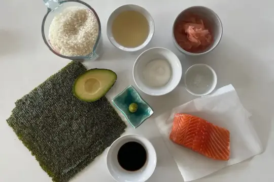 Wszystkie składniki do sushi: ryż, nori, łosoś, awokado, sos sojowy, wasabi, marynowany imbir i ocet ryżowy.