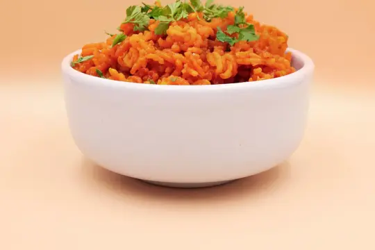 Pomarańczowy ryż z curry, posypany świeżą natką pietruszki, w białej miseczce.