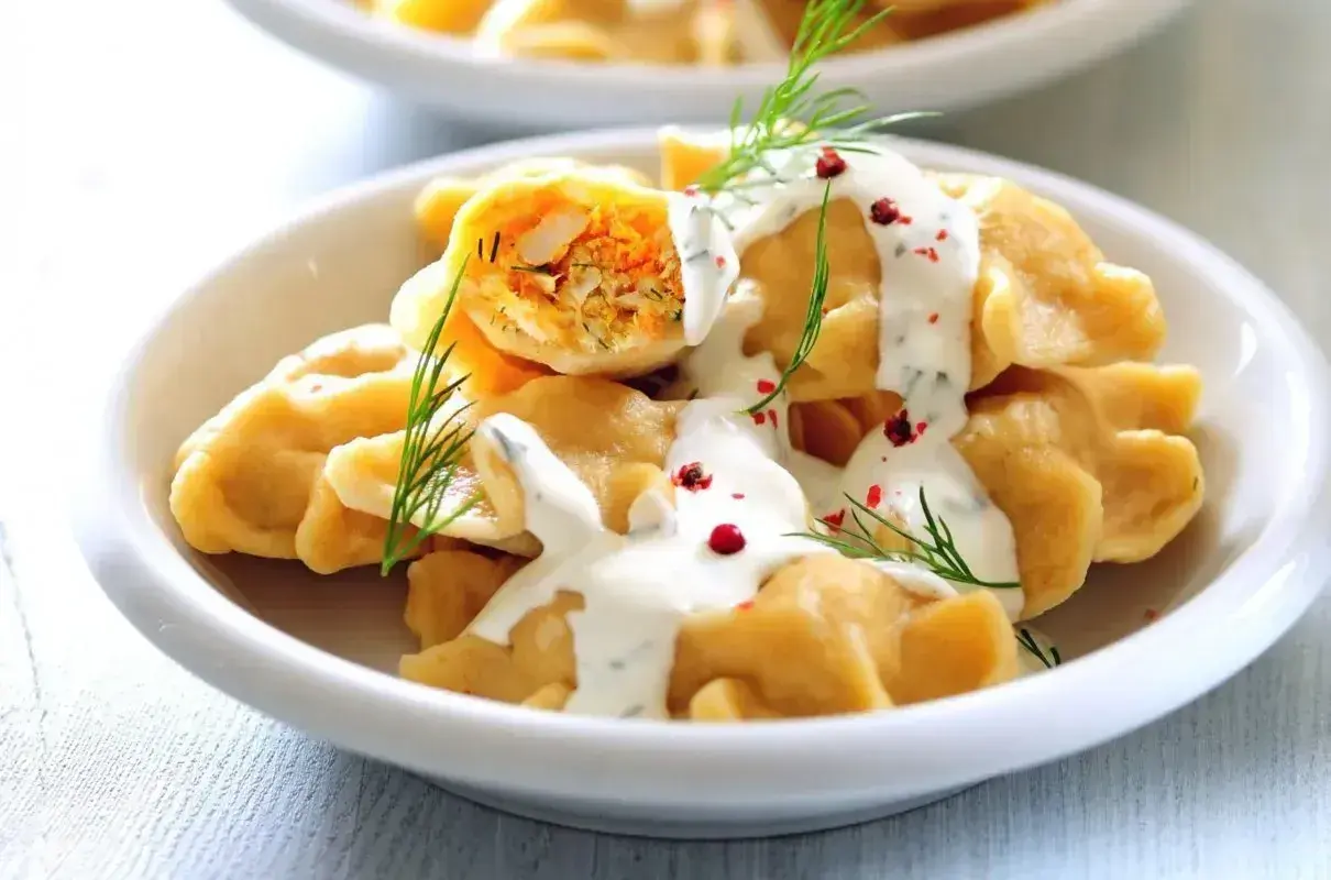Pierogi z farszem, polane sosem, udekorowane koperkiem i pieprzem.