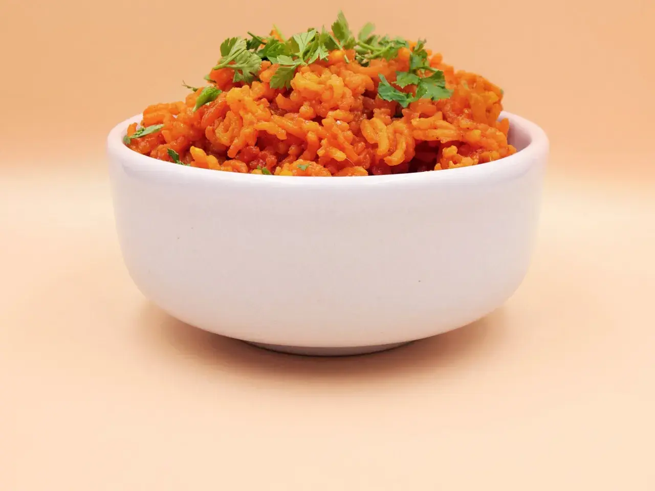 Pomarańczowy ryż z curry, posypany świeżą natką pietruszki, w białej miseczce.