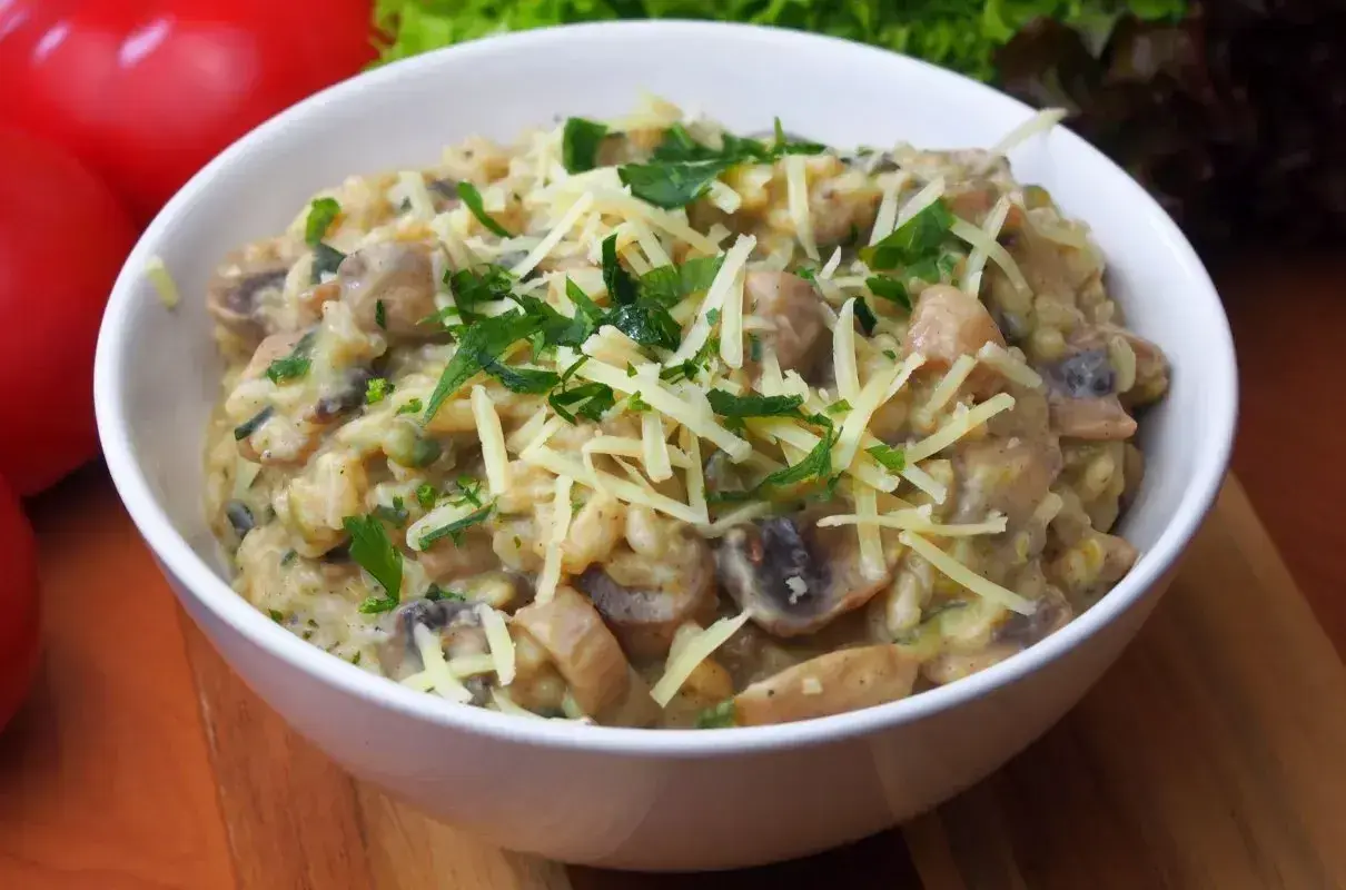 Pyszne risotto z pieczarkami, posypane startym serem i świeżą natką pietruszki, czeka w białej miseczce.