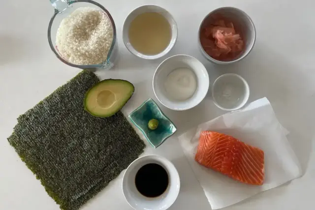 Wszystkie składniki do sushi: ryż, nori, łosoś, awokado, sos sojowy, wasabi, marynowany imbir i ocet ryżowy.